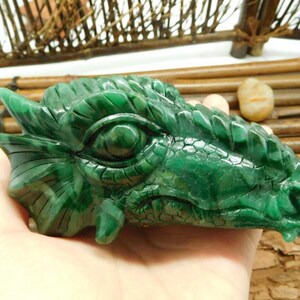 Puede incluir: Una cabeza de drag&oacute;n verde tallada en jade. Los ojos del drag&oacute;n est&aacute;n abiertos y su boca est&aacute; ligeramente abierta. Las escamas del drag&oacute;n son visibles en su cabeza y cuello.