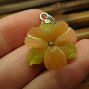 Puede incluir: Un colgante de flor tallada en jade naranja y verde con un aro de plata.