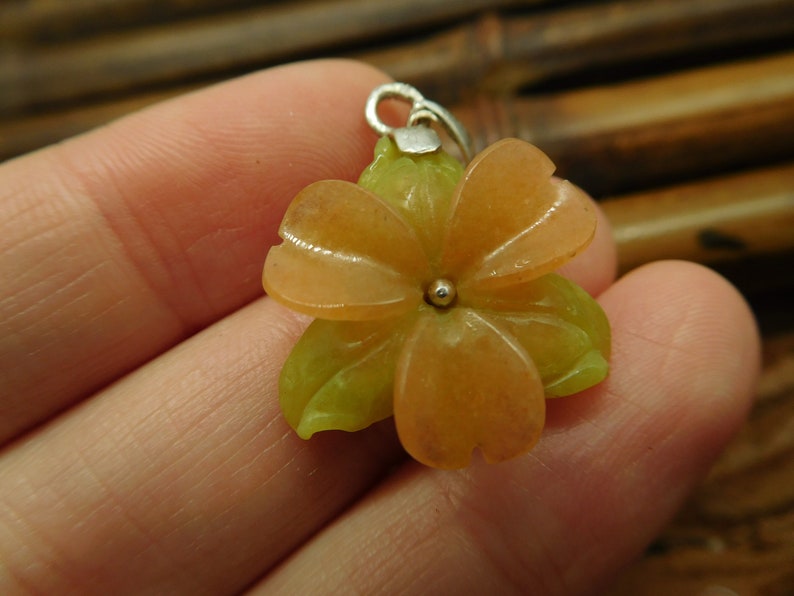 Puede incluir: Un colgante de flor tallada en jade naranja y verde con un aro de plata.