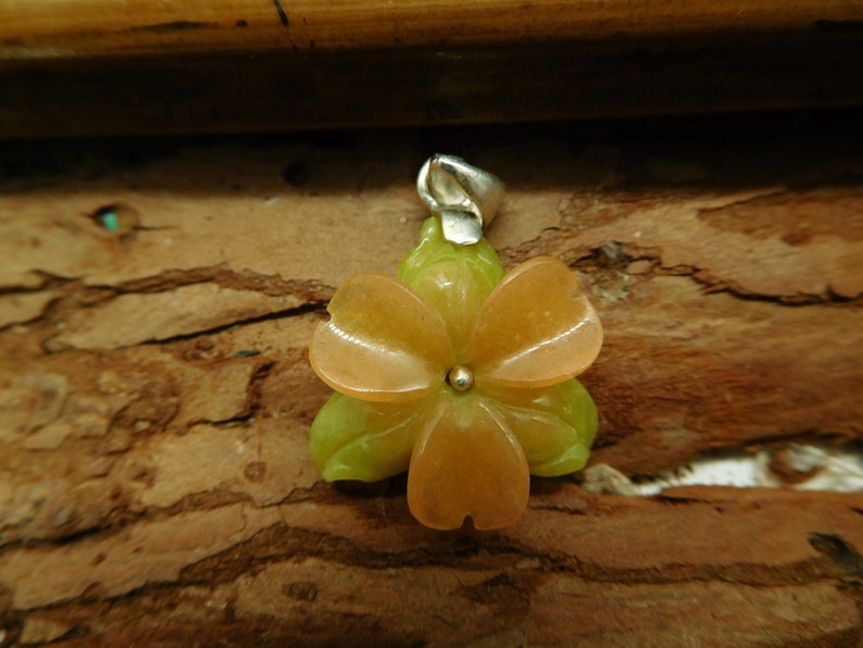 Puede incluir: Un colgante de flor de color melocot&oacute;n tallado en piedra con detalles verdes. El colgante tiene una anilla de plata.