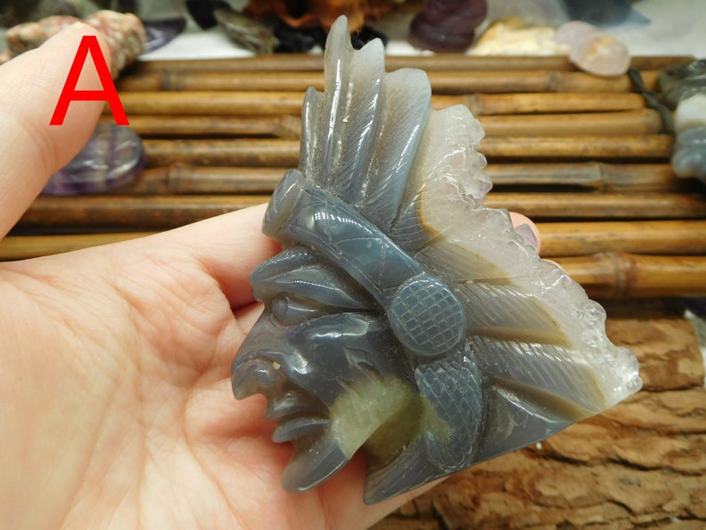 Puede incluir: Una escultura tallada en piedra de &aacute;gata de un jefe nativo americano con tocado. La escultura es gris y blanca con una talla detallada de la cara y las plumas del jefe.