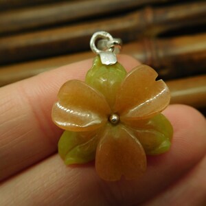 Puede incluir: Un colgante de plata con una flor tallada con p&eacute;talos rosas y verdes. La flor est&aacute; hecha de piedra y tiene una cuenta de plata en el centro.