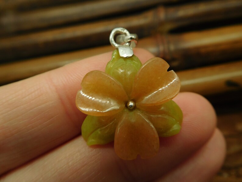 Puede incluir: Un colgante de plata con una flor tallada con p&eacute;talos rosas y verdes. La flor est&aacute; hecha de piedra y tiene una cuenta de plata en el centro.