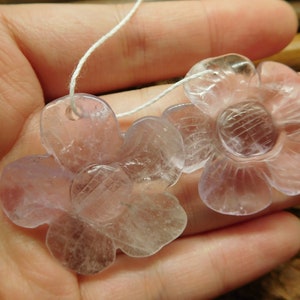 May include: Two translucent lavender flower-shaped pendants with a white string threaded through the top hole of each pendant.