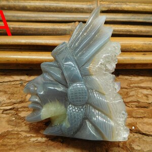Puede incluir: Una escultura tallada en piedra de &aacute;gata gris de la cabeza de un jefe nativo americano con un tocado de plumas. La piedra tiene una formaci&oacute;n de cristal natural en el lateral.