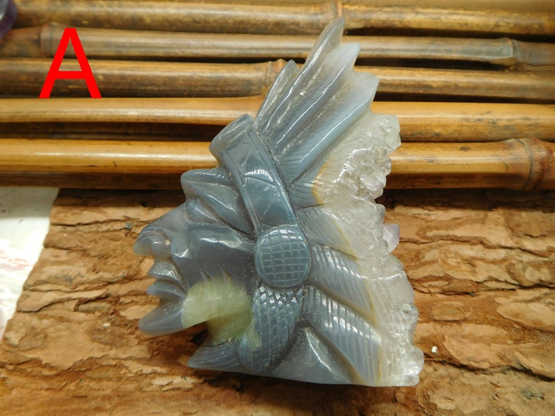 Puede incluir: Una escultura tallada en piedra de &aacute;gata gris de la cabeza de un jefe nativo americano con un tocado de plumas. La piedra tiene una formaci&oacute;n de cristal natural en el lateral.