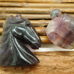 Puede incluir: Dos esculturas de amatista talladas, una cabeza de caballo y una tortuga, sobre un fondo de bambú.