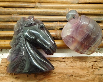 May include: Two carved amethyst sculptures, a horse head and a turtle, on a bamboo background.