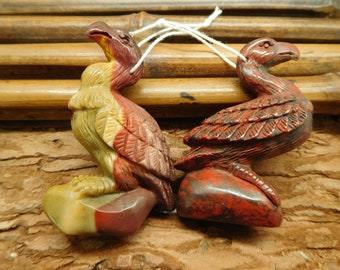 May include: Two carved bird figurines made of red, brown, and yellow jasper. The birds are perched on a rock base.