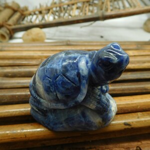 May include: A small blue lapis lazuli turtle sculpture. The turtle is carved in a sitting position with its head turned to the side. The sculpture is detailed with intricate carvings and has a natural, polished finish.