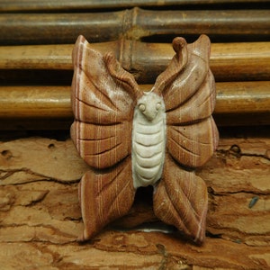 May include: A carved wooden butterfly with brown and white stripes. The butterfly is sitting on a brown wooden surface.