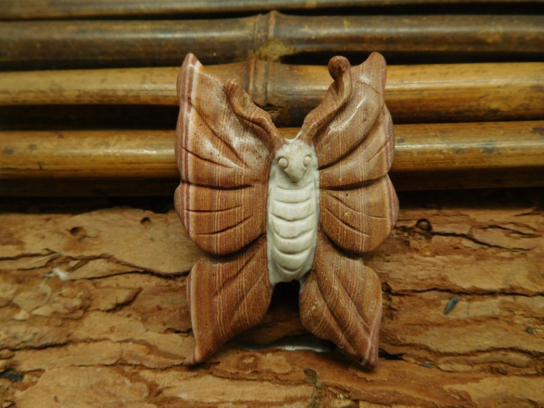 May include: A carved wooden butterfly with brown and white stripes. The butterfly is sitting on a brown wooden surface.