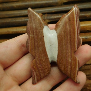 May include: A brown and white butterfly-shaped stone pendant with a layered, striped pattern.