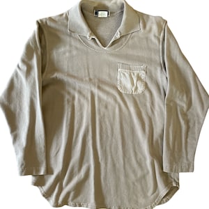 May include: A light brown long-sleeved collared shirt with a single pocket on the left side. The shirt has a relaxed fit and a slightly curved hem.