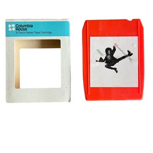 May include: A red 8-track tape cartridge with a white label featuring a black and white image of a person jumping in the air. The label reads "Sly and the Family Stone" and "Fresh". The cartridge is in its original packaging, which is a white box with a blue label that reads "Columbia House 8-Track Stereo Tape Cartridge".