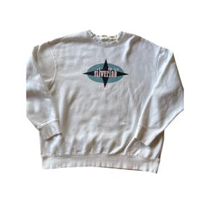 May include: Cream-colored sweatshirt with a crew neck and long sleeves. The front features a teal and black starburst design with the text "silverlab" in a retro font. The sweatshirt has ribbed cuffs and a ribbed hem.