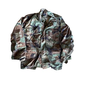 May include: A camouflage jacket with a patch that says "SPEARHEAD" on the left sleeve.