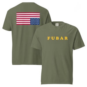 Puede incluir: Camisetas verde oliva. Una camiseta muestra la palabra "FUBAR" en letras amarillas. La otra camiseta tiene un diseño de la bandera estadounidense en la parte superior de la espalda. La bandera tiene rayas rojas y blancas y un cuadrado azul con estrellas blancas.