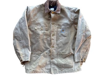 May include: A worn, tan work jacket with a brown corduroy collar. The jacket has multiple pockets, button closures, and a Carhartt logo patch. The fabric shows signs of wear and tear.
