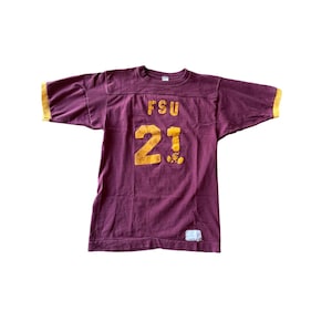 May include: Maroon vintage athletic jersey with gold lettering and trim. The jersey features the letters "FSU" above the number "21" in gold. The sleeves have gold trim. A small white tag is visible near the bottom hem.
