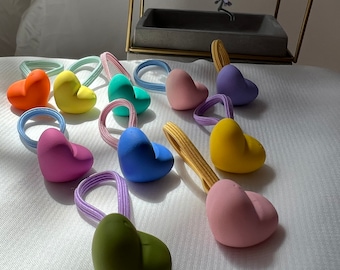 May include: Assortment of colorful heart-shaped hair ties. The hair ties are made of soft, flexible material and come in a variety of colors, including orange, yellow, green, blue, pink, and purple.