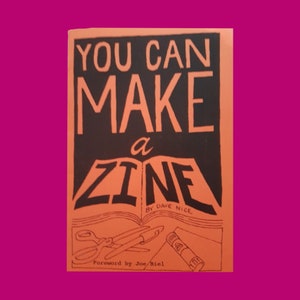 以下が含まれることがあります： デーブ・ナイスによる「You Can Make a Zine」という黒い文字が書かれたオレンジ色の本の表紙。表紙には、開いた本のスタイリッシュなイラストが描かれており、ページには「Zine」という言葉が印刷されています。この本には、ジョー・ビエルによる序文も含まれています。