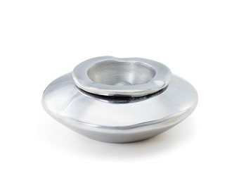 May include: A silver ashtray with a round, slightly indented top and a wider, oval base. The ashtray is made of metal and has a smooth, polished finish.