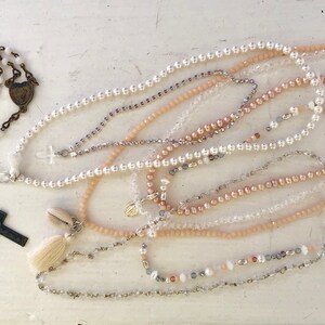 Puede incluir: Una colecci&oacute;n de delicados collares con varios estilos de cuentas, incluyendo acentos de perlas, cristal y conchas. Los collares est&aacute;n dispuestos en capas, creando una est&eacute;tica visualmente atractiva y femenina.