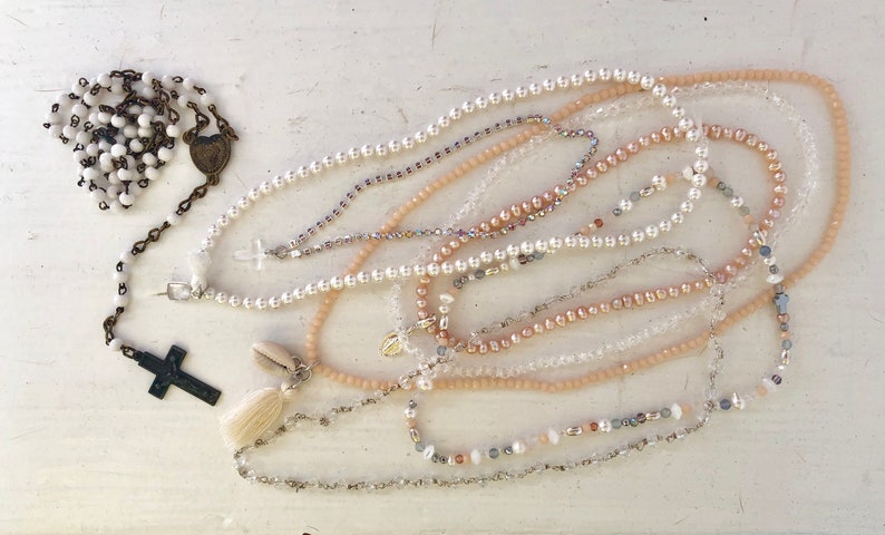 Puede incluir: Una colecci&oacute;n de delicados collares con varios estilos de cuentas, incluyendo acentos de perlas, cristal y conchas. Los collares est&aacute;n dispuestos en capas, creando una est&eacute;tica visualmente atractiva y femenina.