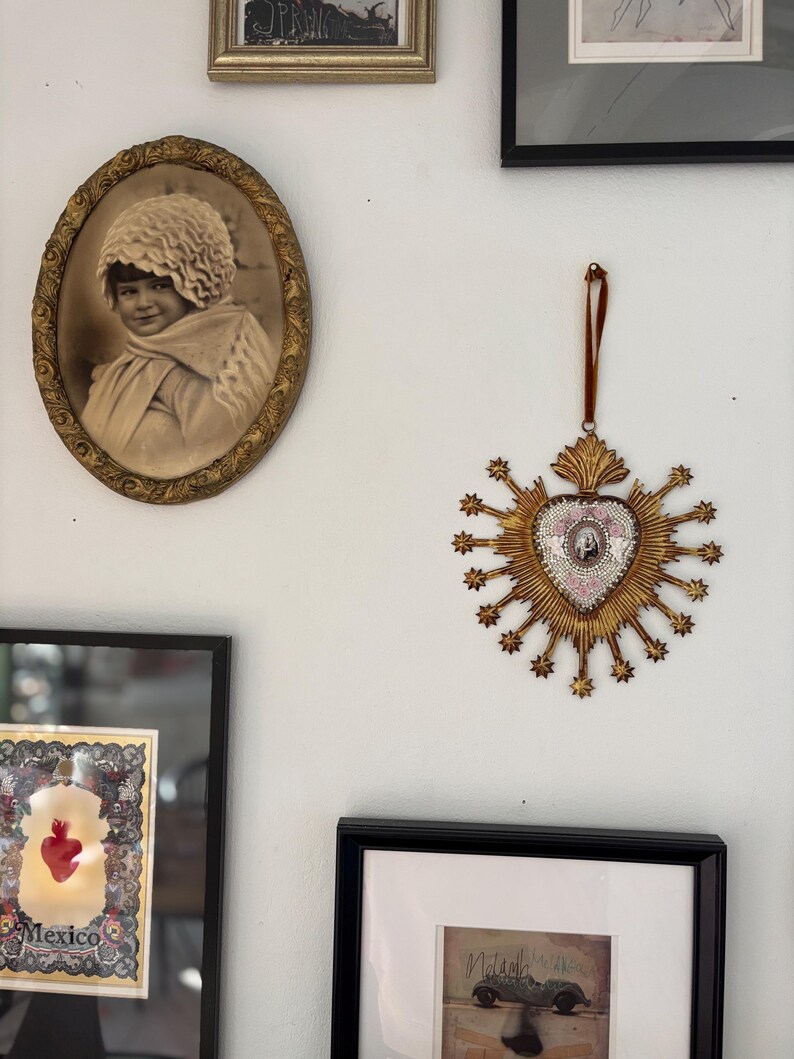 May include: A wall display featuring framed art and decorative pieces. An oval-framed sepia-toned portrait of a child hangs near a gold-colored, starburst-shaped ornament with a central image. Other framed artworks are also visible.