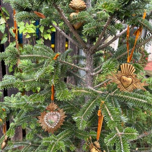 May include: A small Christmas tree decorated with gold-colored ornaments. The ornaments are heart-shaped and sunburst designs, some with the word "LOVE". The ornaments hang from orange velvet ribbons.