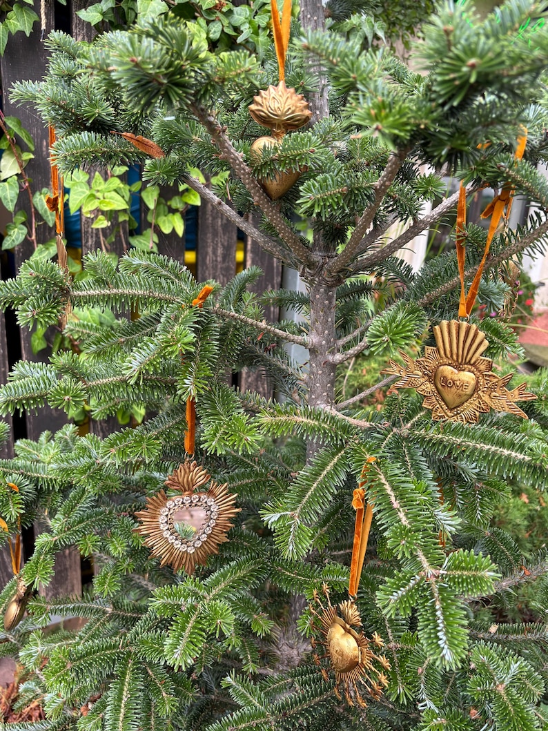 May include: A small Christmas tree decorated with gold-colored ornaments. The ornaments are heart-shaped and sunburst designs, some with the word "LOVE". The ornaments hang from orange velvet ribbons.