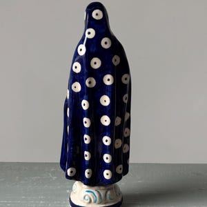 May include: A ceramic figurine of a draped figure, viewed from the back. The figure is primarily dark blue with a pattern of white polka dots. The base is white with blue decorative swirls.