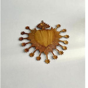 May include: A golden heart-shaped wall hanging with a sunburst design. The heart has a wood grain texture, surrounded by rays and star-shaped accents. A small loop is at the top for hanging. The piece has a vintage or antique aesthetic.
