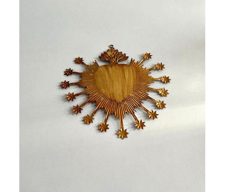 May include: A golden heart-shaped wall hanging with a sunburst design. The heart has a wood grain texture, surrounded by rays and star-shaped accents. A small loop is at the top for hanging. The piece has a vintage or antique aesthetic.