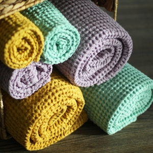 May include: A basket filled with rolled up waffle weave towels in yellow, green, and purple.