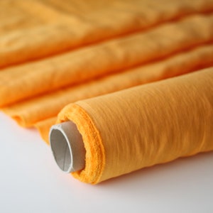 Könnte beinhalten: Eine Rolle aus leuchtend orangefarbenem Stoff, wahrscheinlich Leinen oder Baumwolle, ist auf einer Papprolle aufgerollt. Der Stoff hat eine leicht strukturierte Oberfläche.