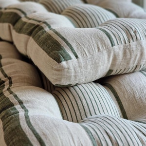 Puede incluir: Primer plano de un cojín blanco y verde a rayas con un diseño capitoné. El cojín está hecho de una tela suave y texturizada.