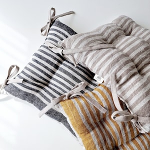 Puede incluir: Tres cojines de silla de lino a rayas con lazos. Los cojines son en blanco y negro, beige y blanco, y amarillo mostaza y blanco.