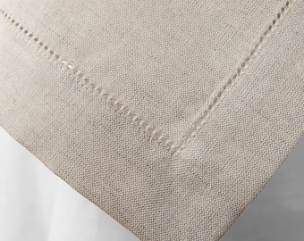 Op de afbeelding: Close-up van een beige linnen tafelkleed met een gestikte rand. De stof heeft een subtiele textuur en voelt licht ruw aan.
