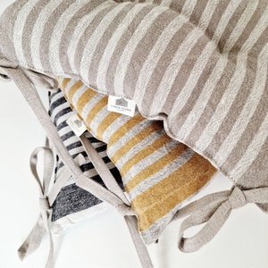 Puede incluir: Tres cojines de silla de lino a rayas con lazos. Los cojines son de color gris y blanco, negro y blanco, y amarillo y blanco. Los cojines tienen una etiqueta "Linen Home".