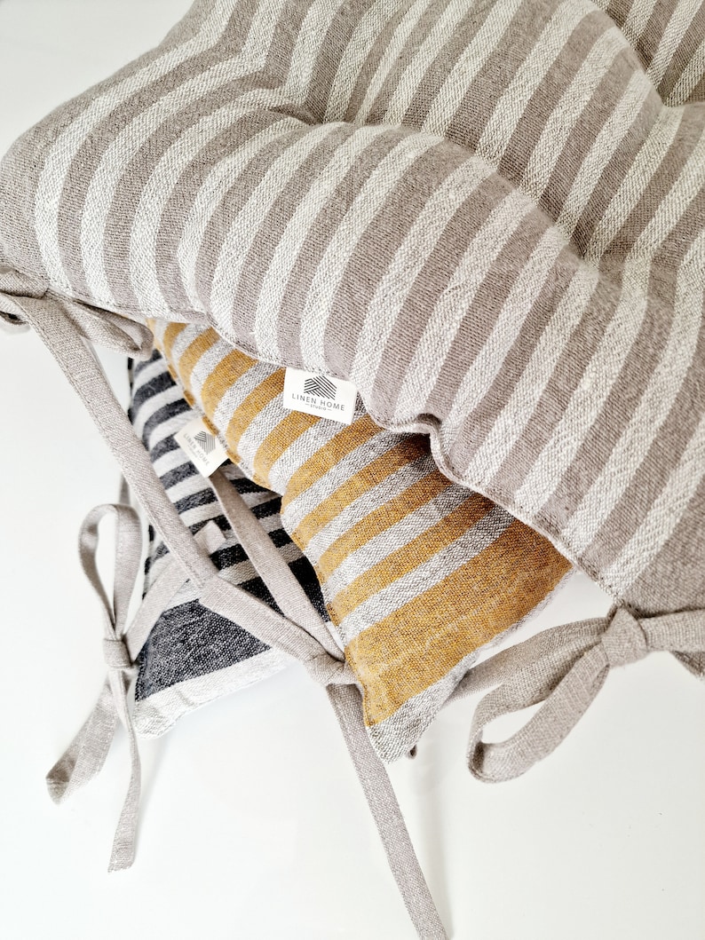 Puede incluir: Tres cojines de silla de lino a rayas con lazos. Los cojines son de color gris y blanco, negro y blanco, y amarillo y blanco. Los cojines tienen una etiqueta "Linen Home".