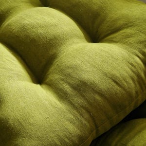 May include: Close-up of a tufted, lime green cushion. The fabric has a textured appearance, with visible weave details. The cushion is a solid color, with a slightly uneven surface due to the tufting. The overall aesthetic is simple and natural.