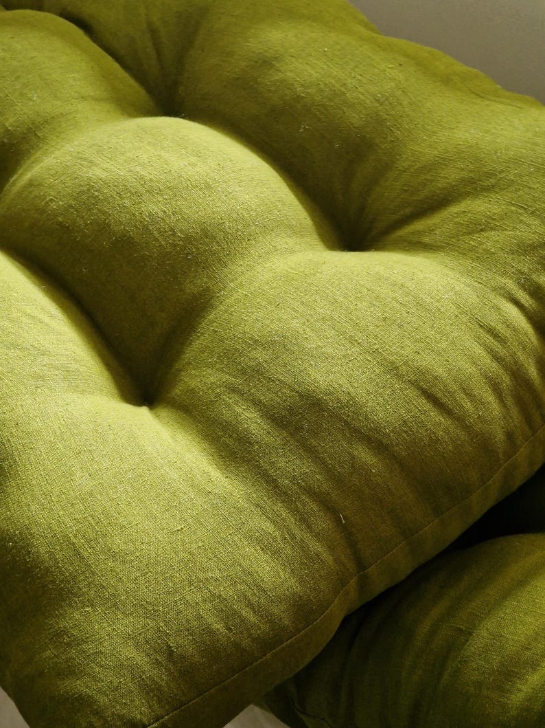 May include: Close-up of a tufted, lime green cushion. The fabric has a textured appearance, with visible weave details. The cushion is a solid color, with a slightly uneven surface due to the tufting. The overall aesthetic is simple and natural.