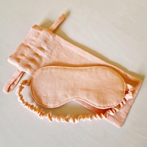 Peut inclure: Un masque de sommeil p&ecirc;che et une pochette assortie avec cordon de serrage. Le masque est de forme arrondie avec un &eacute;lastique souple. La pochette est rectangulaire avec une petite boucle. L'ensemble est en tissu textur&eacute;.