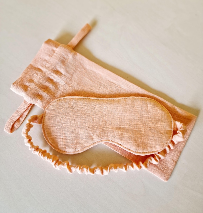 Peut inclure: Un masque de sommeil p&ecirc;che et une pochette assortie avec cordon de serrage. Le masque est de forme arrondie avec un &eacute;lastique souple. La pochette est rectangulaire avec une petite boucle. L'ensemble est en tissu textur&eacute;.