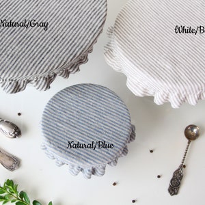 Three striped linen bowl covers showing available patterns: Natural/Gray, Natural/Blue, and White/Beige. Reusable fabric dish covers with elastic ruffles, displayed with vintage silverware. Zero waste kitchen storage options for eco-conscious homes.