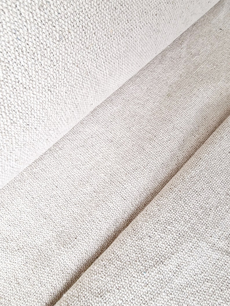 Pu&ograve; includere: Primo piano di un tessuto bianco sporco strutturato con trama visibile. Il tessuto &egrave; piegato, creando linee diagonali e ombre. Il materiale sembra essere una fibra naturale, forse lino o cotone, adatto per tappezzeria o abbigliamento.