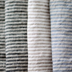 Pu&ograve; includere: Primo piano di tre campioni di tessuto con strisce di colori diversi. I campioni sono una striscia grigio scuro e bianca, una striscia marrone chiaro e bianca e una striscia blu chiaro e bianca.