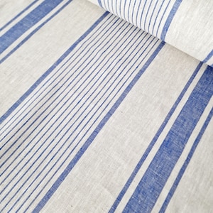 Close-up of oatmeal-colored heavyweight linen fabric with vibrant royal blue grain sack stripes. The 100% natural flax linen is shown folded to highlight its thick, rustic texture and high-quality weave. Ideal for farmhouse style tablecloths, runners, or custom home decor